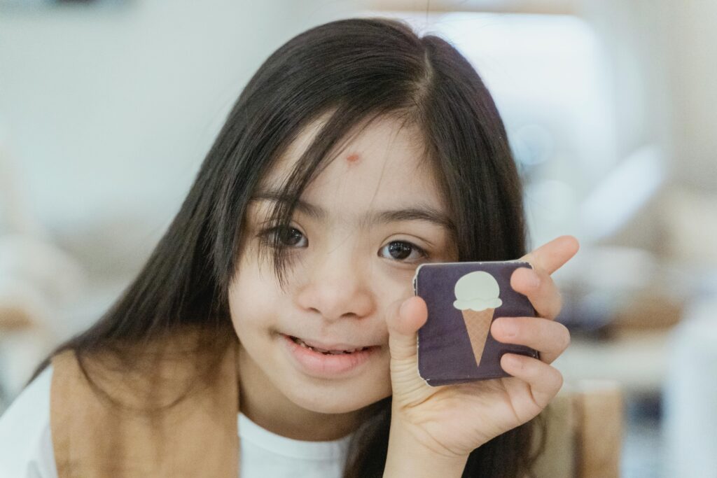 Young girl with Down syndrome smiling and holding a memory game card indoors.
