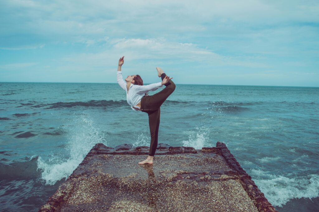 A person practices a high-level yoga pose on a pier by the ocean, capturing serene balance.